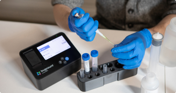 gloved hands using a pipette to put fluid into a tube