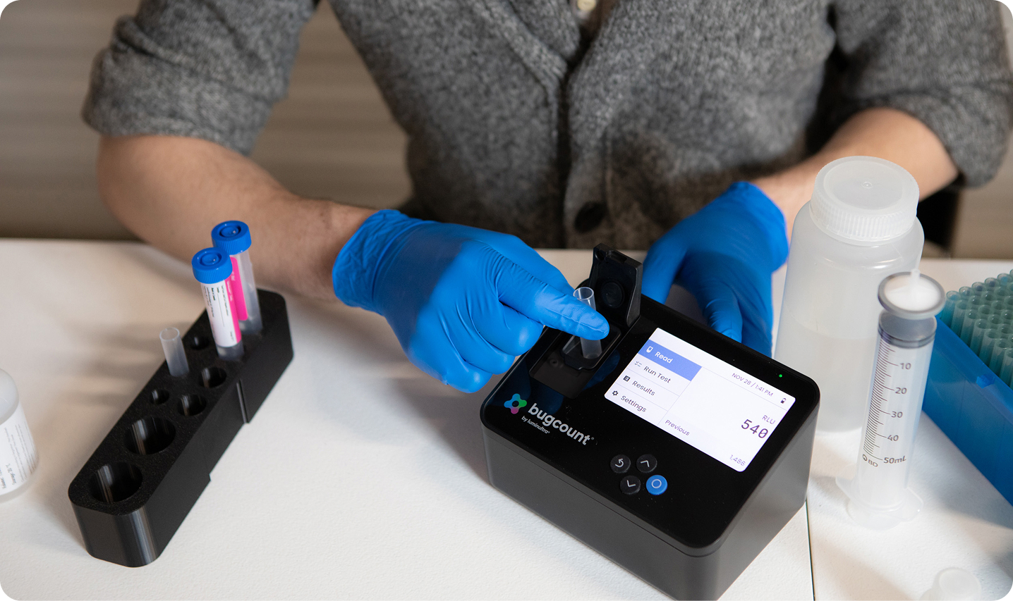 person with gloved hands putting tube into bugcount analyzer device